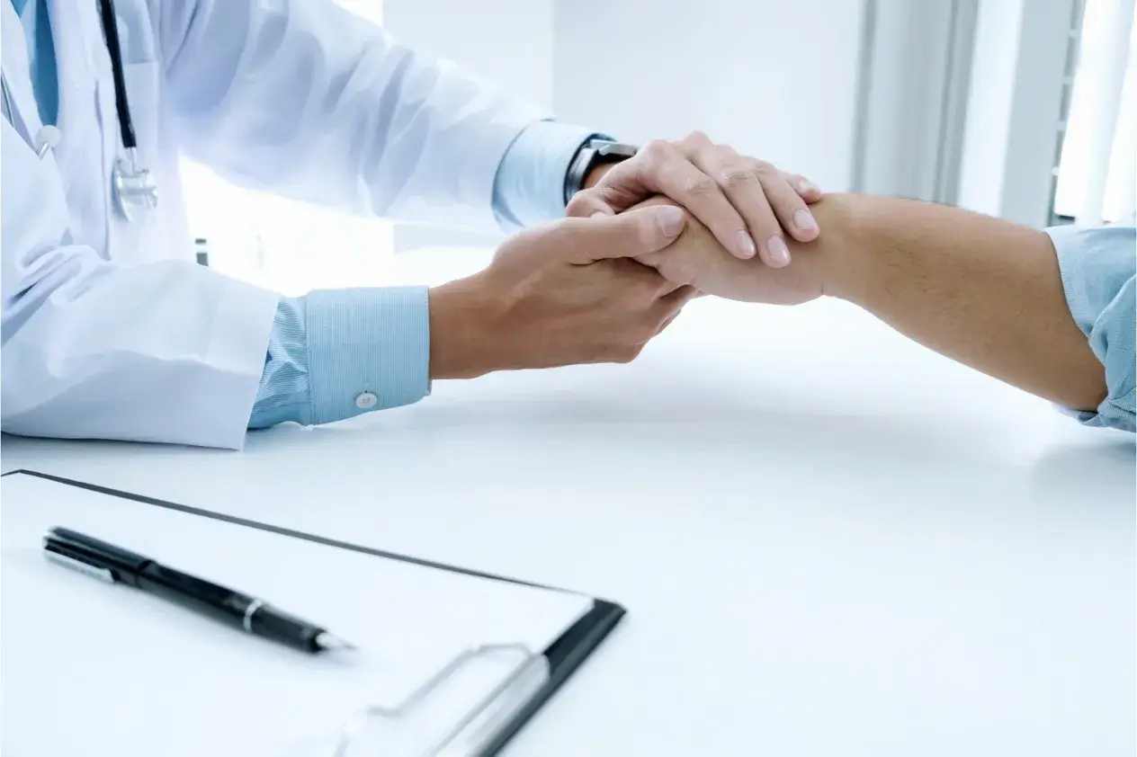 A person wearing a stethoscope holding another person’s hand across a desk