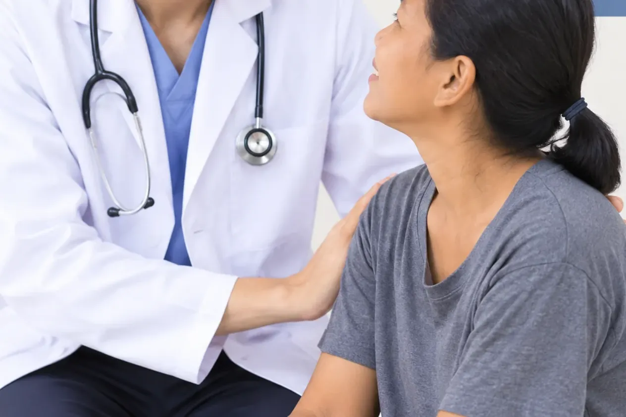 Person in a white coat resting a hand on a seated woman’s shoulder